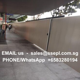 Construction barrier along a sidewalk with large white text displaying contact information (email and phone/WhatsApp) for sales.